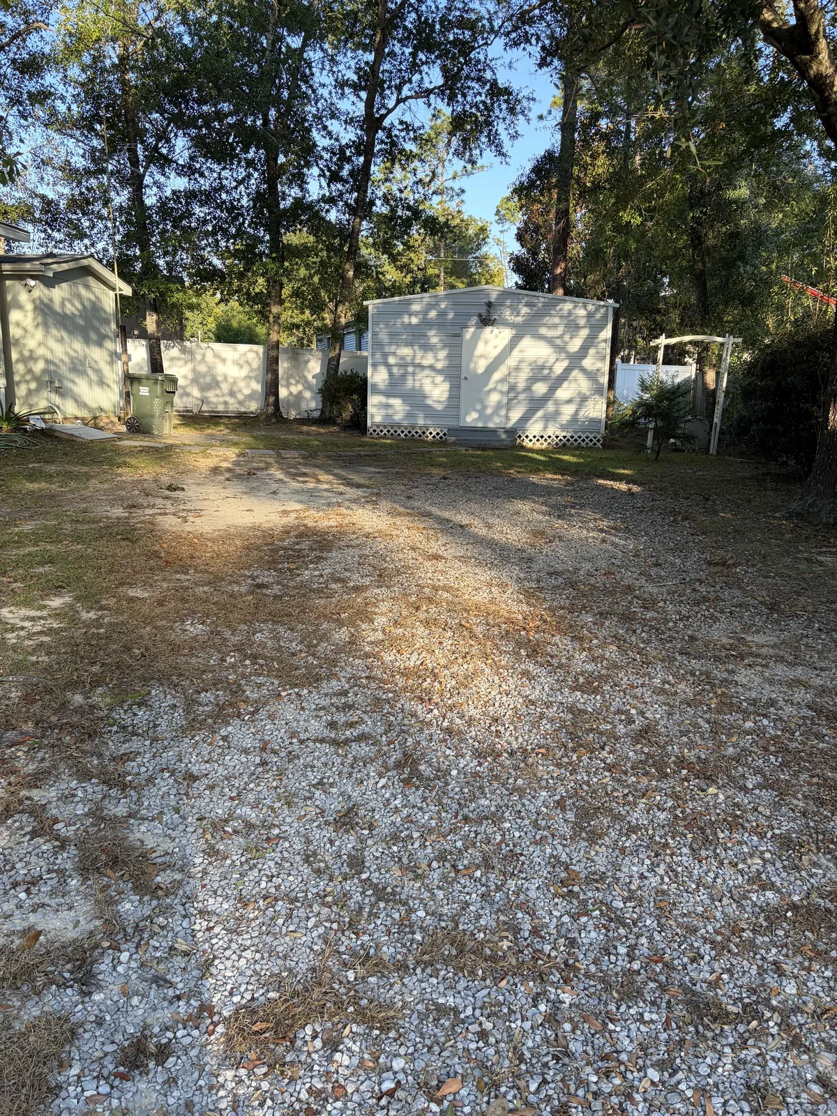 A gravel drive beside a storage shed, the old stone thinned to patches with grass coming through, before the rehab