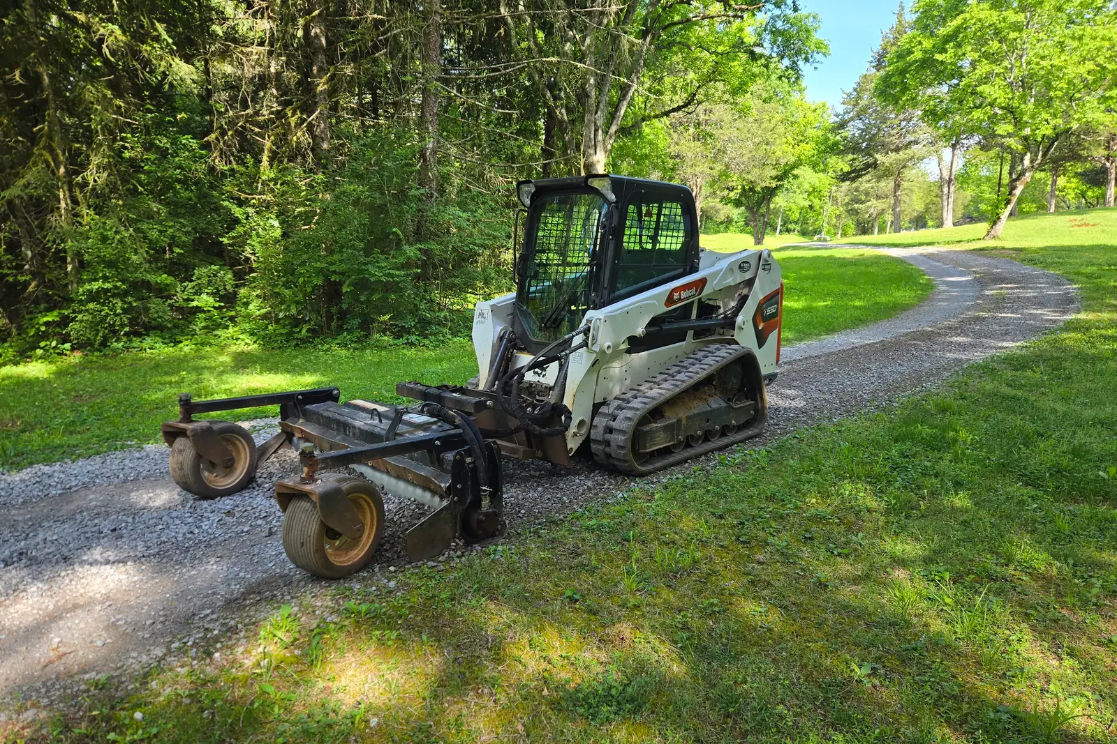 Compact track loader with a rake attachment grading a gravel driveway